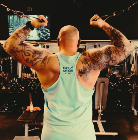 Muskulöser Mann mit tätowierten Armen zieht Kabel im Fitnessstudio.