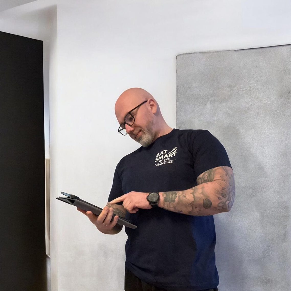 Lächelnder Mann in grauer Kapuzenjacke steht in einem modernen Fitnessstudio.