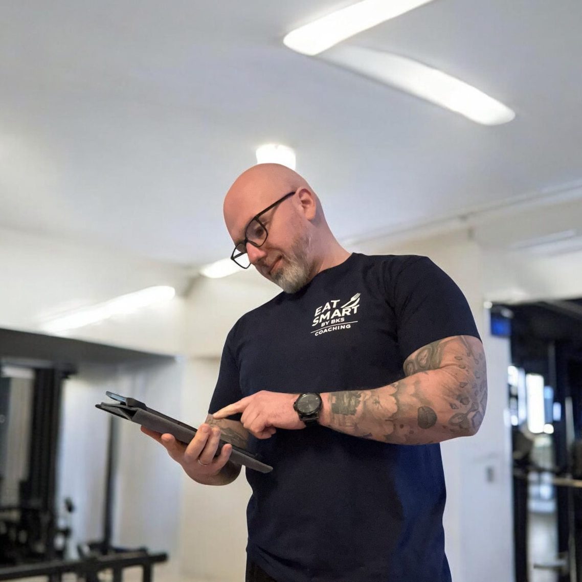 Lächelnder Mann in grauer Kapuzenjacke steht in einem modernen Fitnessstudio.
